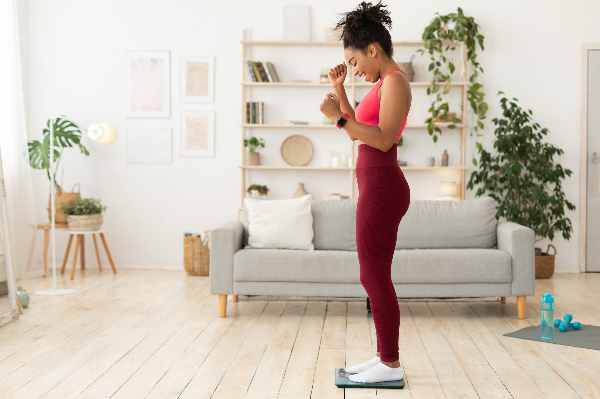 Nicety Wellness - Joyful Black Woman Weighing Herself After Successful Weight Loss Indoors